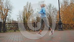 Fit blonde woman runnning in autumn park.