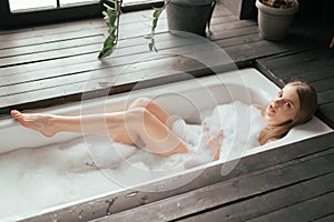 Fit body beautiful blonde young woman taking bath with bubbles in bathroom interior with plenty green plans