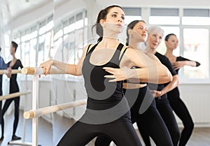 Fit brunette practicing demi plie at barre at ballet class