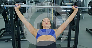 Fit brunette sportswoman lifting heavy barbell lying on bench at the gym