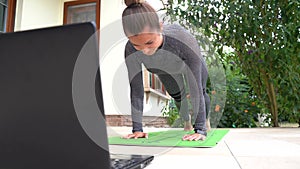 Fit Caucasian woman learning downward facing dog pose on laptop in backyard