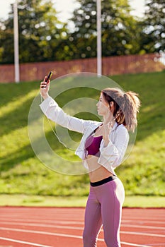 Fit caucasian woman is making selfies at outdoor stadium on a sunny summer day