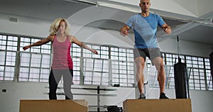 Fit caucasian woman and man jumping on pylo boxes at the gym