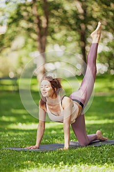 Fit caucasian woman practising yoga in a summer park