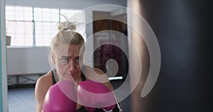 Fit caucasian woman wearing boxing gloves training with punching bag at the gym