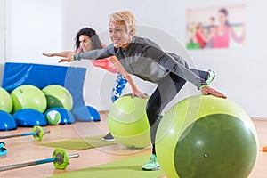 Fit Caucasian women doing crane exercise standing on one leg with their arms out to sides holding on to balance ball