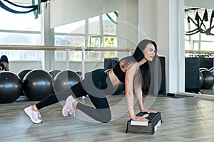 Fit caucasian young woman in sportswear doing step aerobics exercise at fitness studio