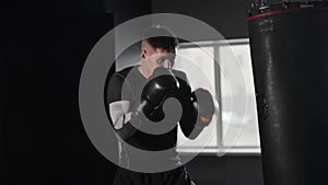 Fit and concentrated young man boxer hitting the punching bag in the gym