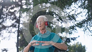 Fit confident senior sportsman training outdoors in summer spring park listening to music in headphones. Portrait of