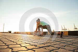 Fit and confident woman in starting position ready for running. Female athlete about to start a sprint looking away.