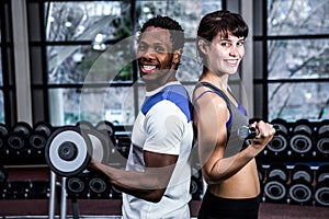 Fit couple lifting dumbbells back to back