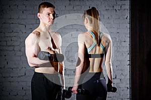 Fit couple lifting dumbbells together at the gym.