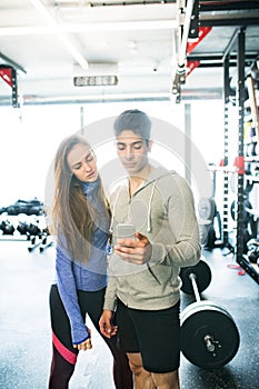 Fit couple in modern crossfit gym with smartphone.