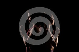 Fit couple posing together. Boy and girl praying back to back side lit silhouettes on black background