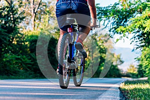 Fit cyclist rides his bicycle bike on an empty road in nature wearing a baseball hat and red t-shirt