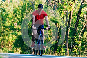 Fit cyclist rides his bicycle bike on an empty road in nature wearing a baseball hat and red t-shirt