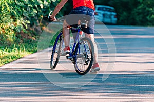 Fit cyclist rides his bicycle bike on an empty road in nature wearing a baseball hat and red t-shirt