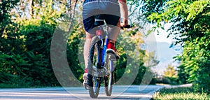 Fit cyclist rides his bicycle bike on an empty road in nature wearing a baseball hat and red t-shirt