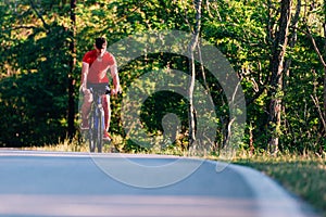 Fit cyclist rides his bicycle bike on an empty road in nature wearing a baseball hat and red t-shirt