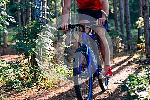 Fit cyclist riding his bike downhill through a forest  woods  while wearing a red shirt and red shoes