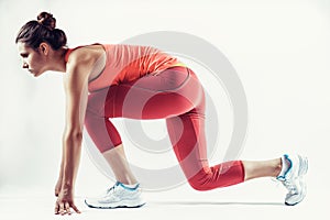 Fit female athlete ready to run over grey background. Female fitness model preparing for a sprint