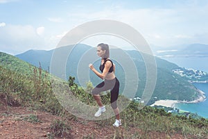 Fit female jogger exercising, running uphill with sea and mountains in background
