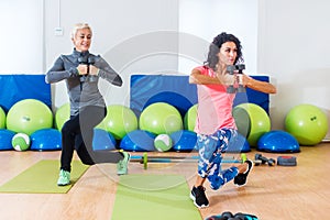 Fit female sportswoman doing curtsy lunge exercise with dumbbells in group fitness studio class