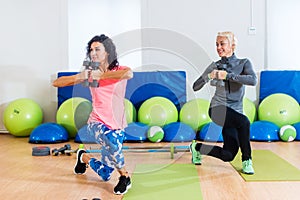 Fit female sportswoman doing curtsy lunge exercise with dumbbells in group fitness studio class