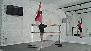 Fit female stretching on gymnastic barre indoors