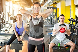 Fit friends working out together with kettle bells in gym.