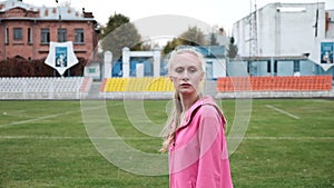 Fit girl in activewear stands outdoors in the middle of stadium before fitness