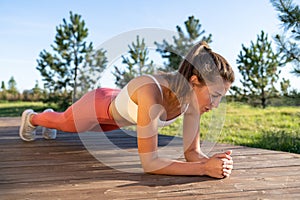 Fit girl do plank on elbows working out outdoor in park at summer day. Endurance motivation concept