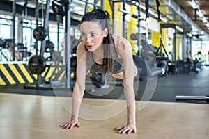 Fit girl doing plank exercise for back spine and posture. Woman doing push-ups while legs hanging on elastic rope in gym