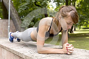 Fit girl doing plank exercise outdoor in the park warm summer day. Concept of endurance and motivation