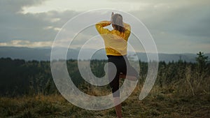 Fit girl exercising yoga pose in mountains. Lady standing in tree pose on grass