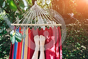 Fit girl is lying in the colourful hammock. Woman with beautiful legs is relaxing in hippie style garden near the village house.