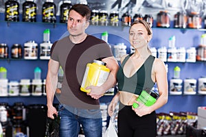 Fit girl and sport guy carrying jars with food supplements in store