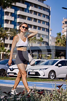 fit girl in sportswear goes to morning workout at park, carrying yoga mat holds bottle of water. Sporty caucasian