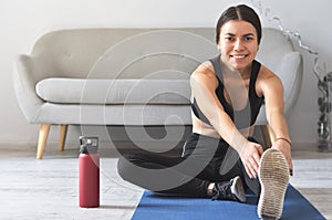 Fit girl stretching her leg to warm up on blue mat at home. Fitness concept, close up on sport shoes