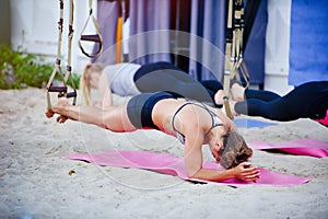 Fit girls in the gym doing exercises on the board for the spinal column and posture. Beautiful young sports people work with TRX i