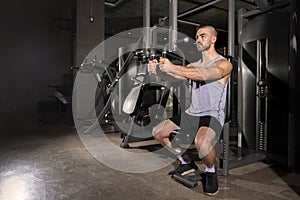 Fit handsome man exercising with machine at sport gym. Fitness and workout concept
