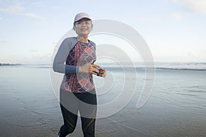 Fit and happy middle aged woman running on the beach - 40s or 50s attractive mature lady with grey hair doing jogging workout