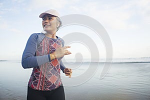 Fit and happy middle aged woman running on the beach - 40s or 50s attractive mature lady with grey hair doing jogging workout