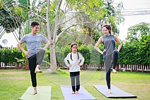 Fit happy people working out outdoor. Family Asian parent and child daughter exercising together on a yoga mat at home garden.