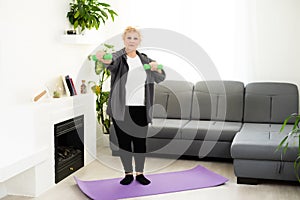 Fit happy senior woman doing stretching exercises on her yoga mat