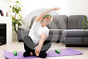 Fit happy senior woman doing stretching exercises on her yoga mat