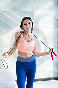 Fit happy woman in sportswear holding jump rope at home in bright room
