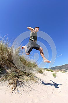 In forma, sani uomo di mezza età saltare o saltare sulle dune di sabbia sulla spiaggia.