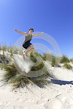 Fit, healthy middle aged man leaping over sand dunes