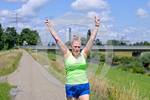 Fit healthy woman cheering as she jogs along a river bank